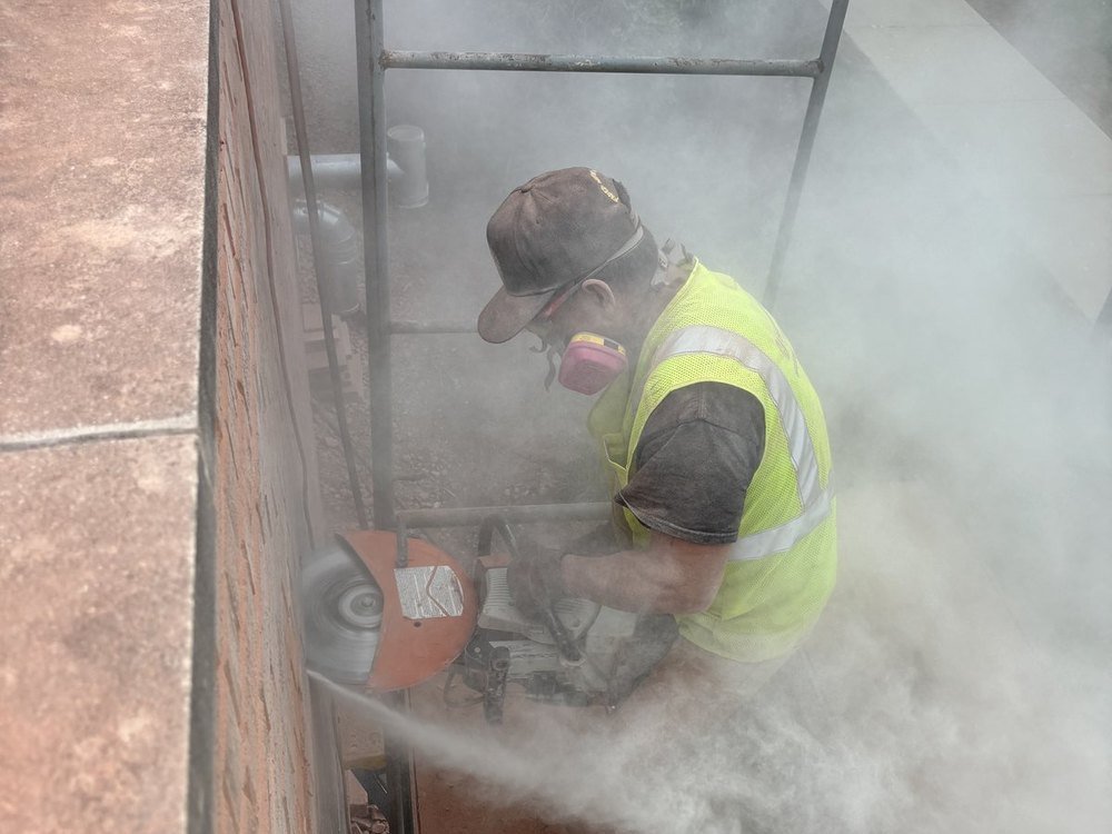 Mason grinding out deteriorated mortar joints in full protective gear